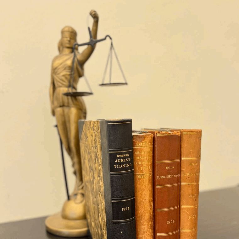 Mässingsfigur av Justitia med våg, bakom en rad äldre inbundna juridiska band från 1924.